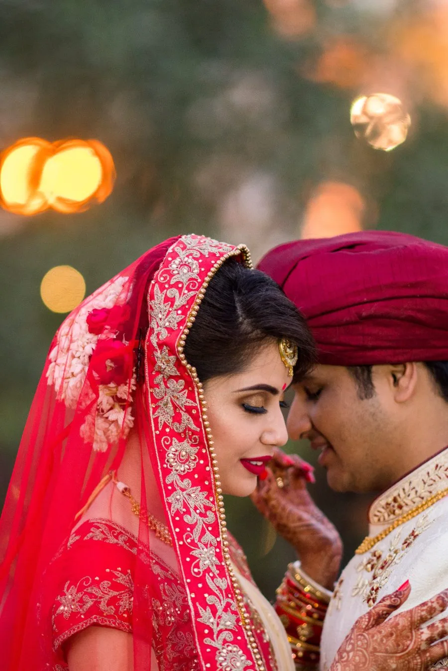 Bride in a red veil resting her forehead against the groom's during the ceremony