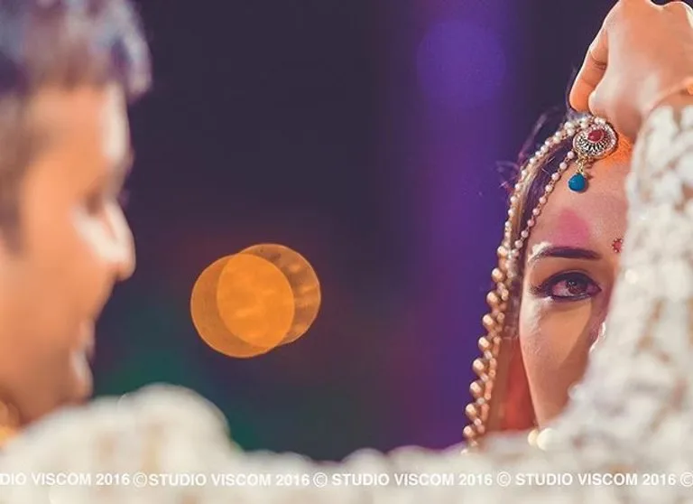Bride in profile during the ceremony, photographed past the groom against evening bokeh