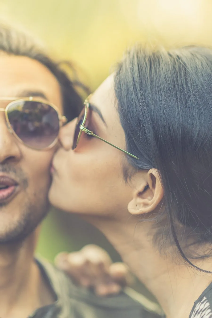 Pre-wedding portrait of a couple in sunglasses, the groom kissing the bride on the cheek