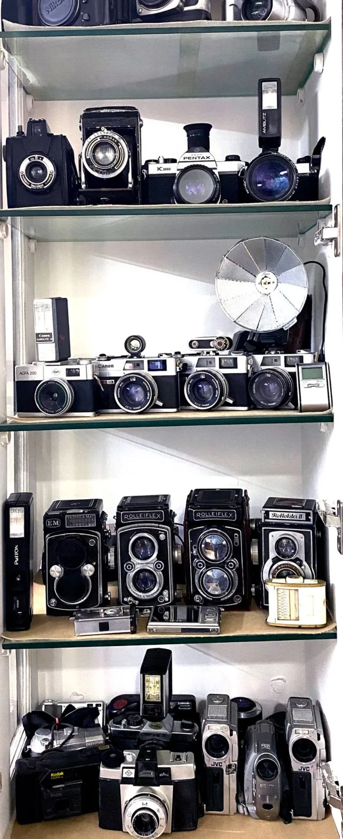Shelves of the studio's camera collection, from 1982 film bodies to current digital cameras